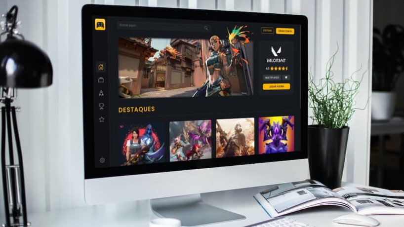 Computador exibindo uma loja de jogos online com destaque para o jogo Valorant na tela inicial. A interface mostra menu lateral à esquerda, banner principal e seção de destaques com outros jogos.