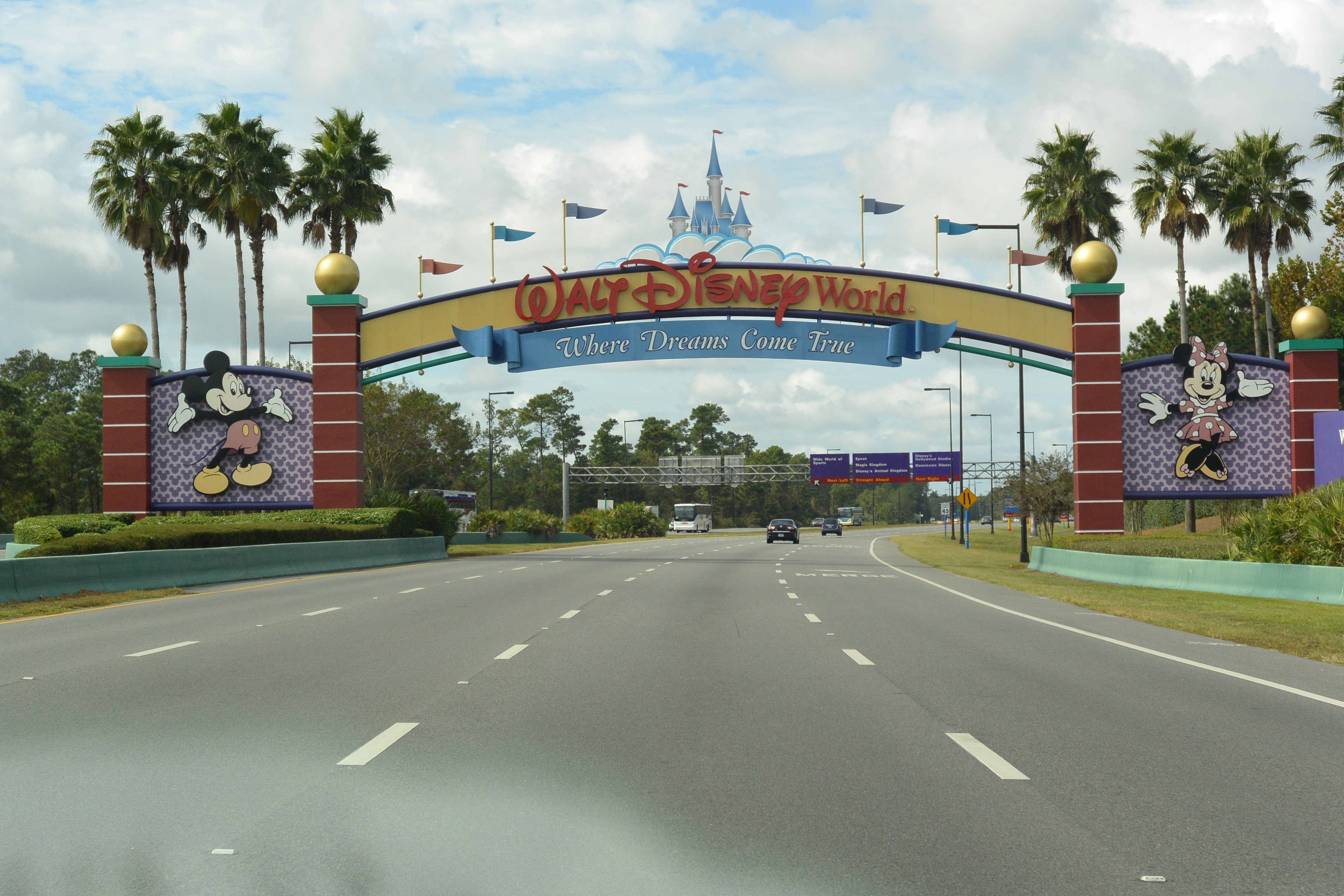 Entrada do Walt Disney World em Orlando, com um grande arco colorido exibindo Mickey e Minnie Mouse e a frase 'Where Dreams Come True' sobre a estrada principal.